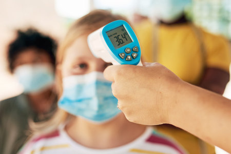 Taking Covid seriously. an unrecognizable woman standing and using a thermometer to check her...
