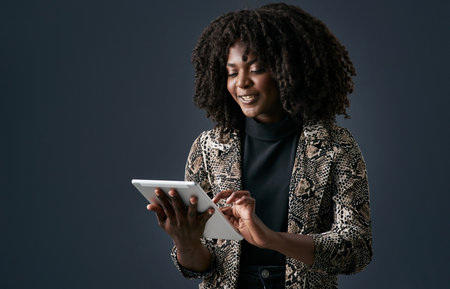 Its important to be able to keep in touch. a young businesswoman using a digital tablet against a studio background.の写真素材