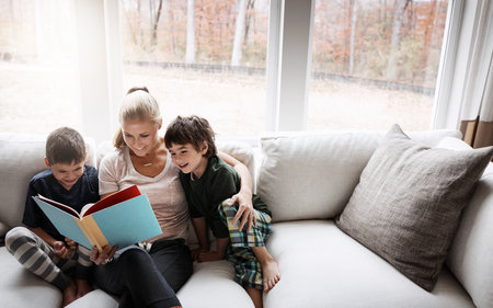 Books, reading and mother with kids on sofa for storytelling time in living room of happy home. Love, learning and woman with children, book and fantasy story on couch, growth and child development.の写真素材