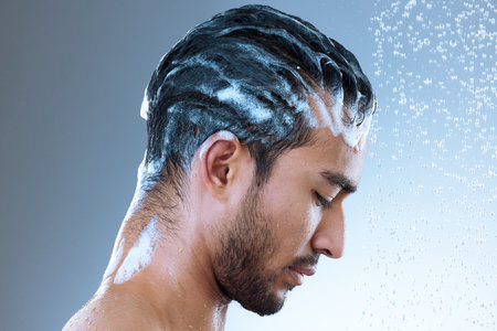 Protect your hair, it is your natural crown. Studio shot of a handsome young man washing his hair in a shower against a grey background.の写真素材