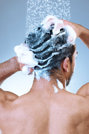Radiate freshness, wherever you go. Rearview studio shot of an unrecognizable young man washing his hair in a shower against a grey background.の写真素材