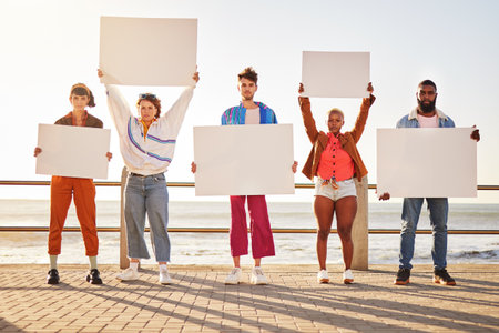 Portrait, poster and diversity with friends together holding signage in protest on the promenade by the sea. Freedom, mockup and billboard with a man and woman friend group holding blank sign boardsの写真素材