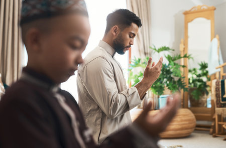 Parents shape the destinies of their children. a young muslim man and his son praying in the lounge at home.の写真素材