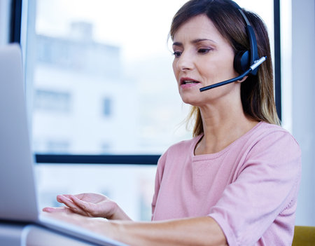 Shes the pro at fielding dozens of calls a day. a mature call centre agent working on a laptop in an...