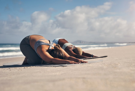 Yoga keeps us physically and mentally fit. two young women practicing yoga on the beach.の写真素材