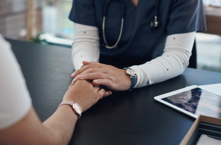 A doctor and a comforter. an unrecognizable doctor holding hands with a patient in an office.