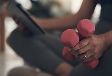 Keeping toned the lockdown way. an unrecognizable woman sitting alone at home and holding dumbbells during a workout.の写真素材