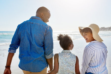 Black family, beach and walking during summer on vacation or happy holiday laughing and enjoying the scenery at the ocean. Sea, water and parents with daughter, child or kid with childhood freedomの写真素材