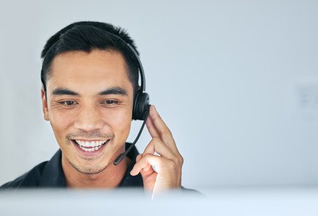 Answering each call with a smile. a handsome young salesman sitting alone in his office and wearing a headset while using his computer.の写真素材
