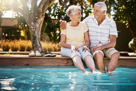 Senior couple, hug and swimming pool for holiday in relax for love or quality bonding time together on summer vacation. Happy elderly man holding woman relaxing with feet in water by the poolsideの写真素材