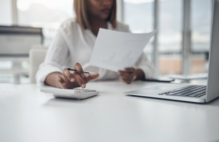 Staying on top of office budgets. an unrecognizable businesswoman sitting alone in her office and using a calculator.の写真素材