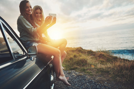 Friends at sunset, women and selfie on beach, travel and adventure on car outdoor, nature and sea holiday. Road trip mockup, happy in picture on summer vacation, smartphone photography and lens flareの写真素材