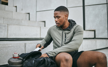 Exercise, workout and black man on stairs, relax and training for fitness, wellness and health. African American male, athlete and looking in bag on steps, outdoor and sportswear for cardio or energyの写真素材