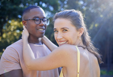 Happy woman, smile and interracial couple for hug, love or care for summer holiday, relationship or bonding in the park. Female holding man smiling in happiness for quality time, romance or embraceの写真素材