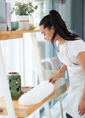 No one likes to see dust on shelves. an attractive young woman standing alone in her home and...