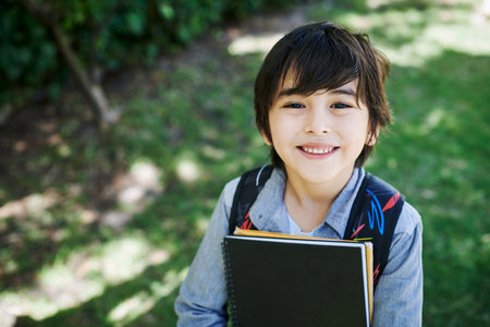 Ready to learn some new things. a little boy wearing a backpack while carrying books in nature.