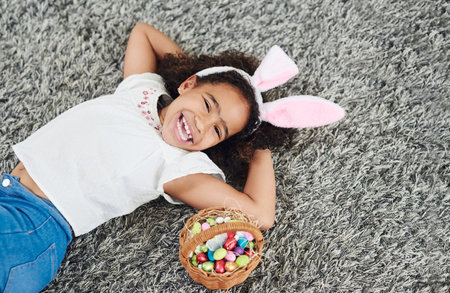 Too the winner goes the spoils. a young girl laying on the floor with a basket of Easter eggs at home.の写真素材