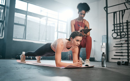 Personal trainer, fitness and clipboard with a black woman coaching a client in a gym during her workout. Health, exercise or training and a female athlete doing a plank with her coach writing notesの写真素材