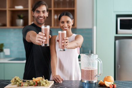 Cheers. Cropped portrait of an affectionate young couple making smoothies in their kitchen at home.の写真素材