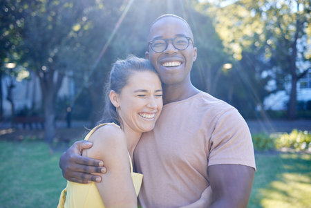 Happy interracial couple, hug and laughing in joy for bonding relationship together in the park. Man hugging woman smiling in happiness for love, embrace and sharing a laugh for funny joke in natureの写真素材