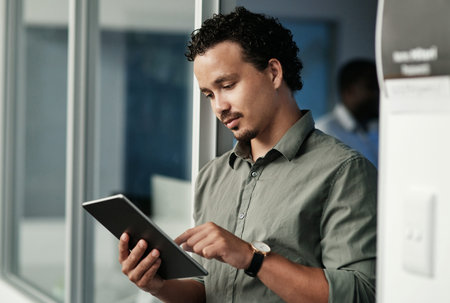 We seem to be on track. a handsome young businessman standing in the office and using a digital...