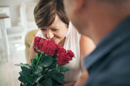 You know how much I love these. a mature wife smelling the bouquet of roses her husband gave her.の写真素材