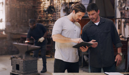 No project is too complicated when we collaborate. two men discussing something on a digital tablet while in their workshop.の写真素材