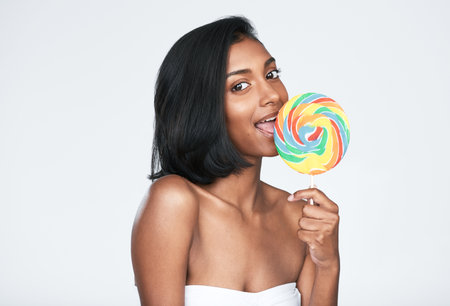We can go natural or we can go colourful. a beautiful woman holding a rainbow lollipop against a white background.の写真素材