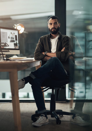 Getting it done is the only option. Portrait of a confident young businessman working late at night in a modern office.の写真素材