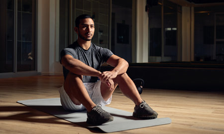 The gym is his fortress of solitude. Full length shot of a handsome young male athlete sitting on an exercise mat in the gym.の写真素材