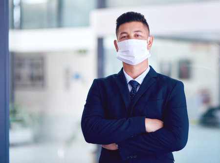A mask is better than a hospital bed. Portrait of a young businessman wearing a face mask in a modern office.の写真素材