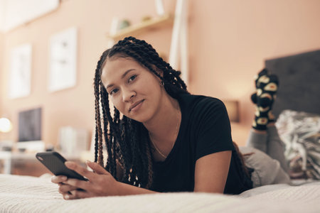 This lockdown, lets all reconnect with our real selves. Portrait of a young woman using a smartphone while relaxing on her bed at home.の写真素材
