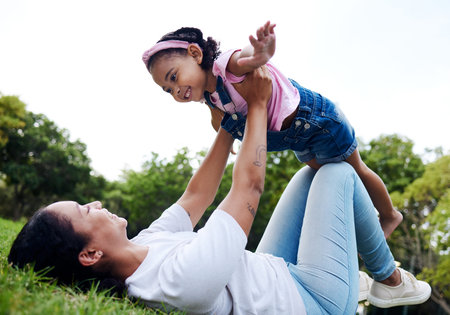 Black family, park and flying with a mother and daughter having fun together while bonding on grass outdoor. Kids, love and nature with a woman and girl playing in a nature garden outside in summerの写真素材