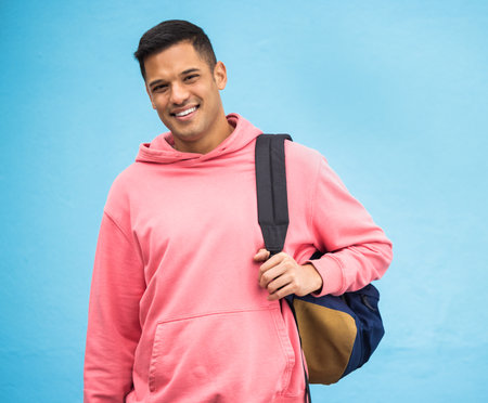 University, student and portrait of man with backpack in studio, happy and smile on blue background. Face, handsome and college student excited about education, vision and career goal while isolatedの写真素材
