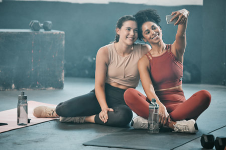 Happy woman, friends and fitness with phone for selfie, moments or picture in workout exercise or training at gym. Sporty women with smile looking at smartphone for photo or healthy wellness togetherの写真素材