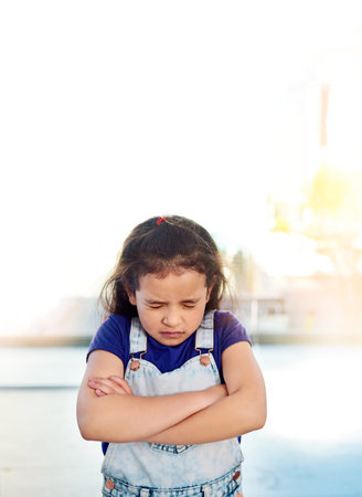 Holding back tears. a sad little girl posing eyes closed and with arms folded at home.の写真素材