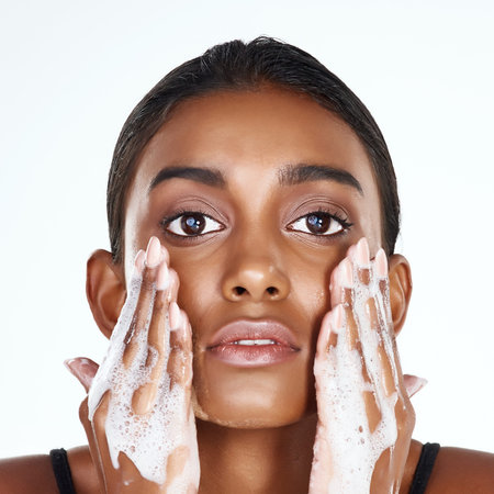 Face everyday the fresh way. Studio shot of a beautiful young woman washing her face against a light...