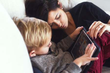 Mommy is falling asleep. a carefree young woman browsing on a digital tablet with her little boy while being seated on a sofa at home during the day.の写真素材