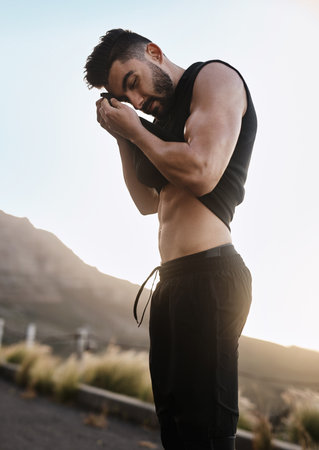 Youve got to sweat in order to sculpt your body. a sporty young man wiping the sweat from his forehead with his top while exercising outdoors.の写真素材