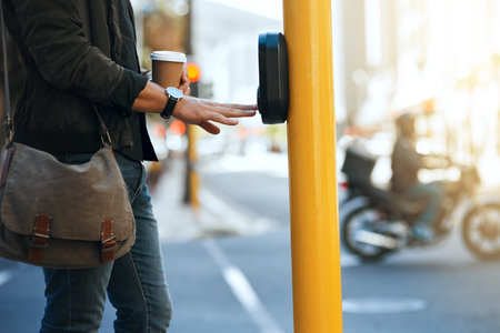 Crossing safely. an unrecognizable man pressing the crosswalk button on a traffic light while...