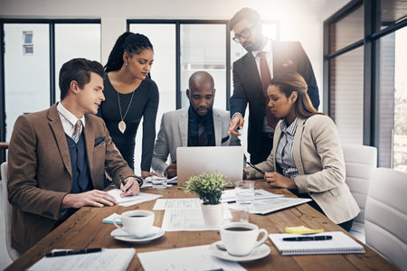 Online resources keep their meetings productive. a group of young businesspeople using a laptop together during a meeting in a modern office.の写真素材