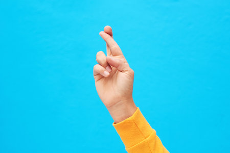 Keeping my fingers crossed. an unrecognizable hand crossing fingers against a blue background.の写真素材