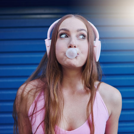 Young girl, bubblegum and headphones, face isolated on blue background, listen to music with freedom...