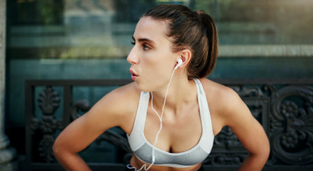 If it motivates you to workout, listen to it. a young woman taking a break from her workout in the city.の写真素材