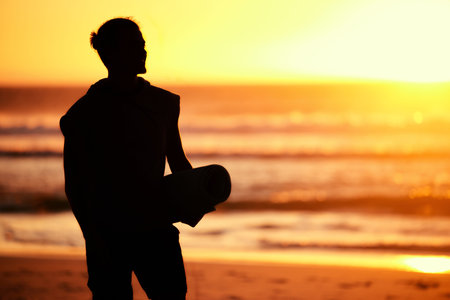 Sunset, silhouette and man with yoga mat at beach getting ready for training. Pilates, zen chakra...