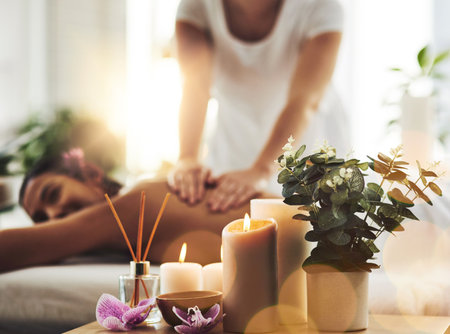 Where the world slows down. spa essentials on a table with a woman getting a massage in the background.の写真素材