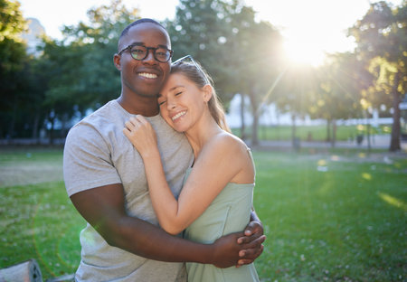 Love, hug or couple of friends in a park on a relaxing romantic date in nature in an interracial relationship. Bonding, black man and happy woman enjoying quality time on a holiday vacation togetherの写真素材