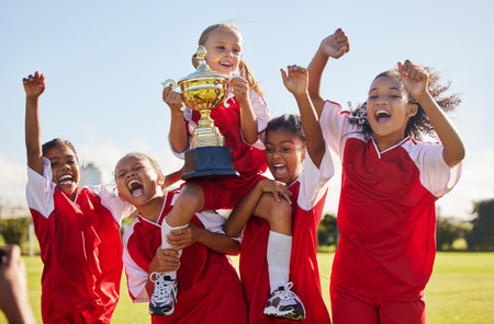 Football, team and trophy with children in celebration together as a girl winner group for a sports competition. Soccer, teamwork and award with sport player kids celebrating success outdoorの写真素材