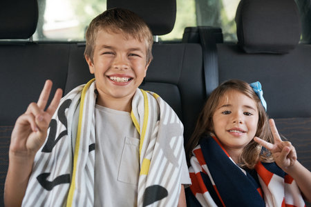 See you later. Cropped portrait of two young siblings sitting in the car and making peace sign...