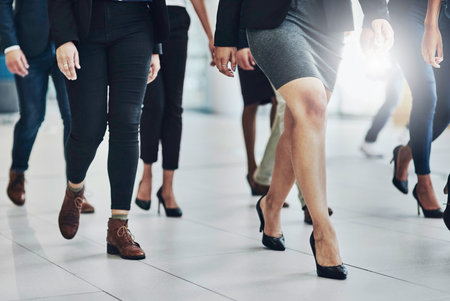 Lets go people. Low angle shot of a group of unrecognizable businesspeople walking together inside of the office at work during the day.の写真素材